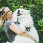 Happy dog owner holding her dog in a clean outdoor space after pet waste removal